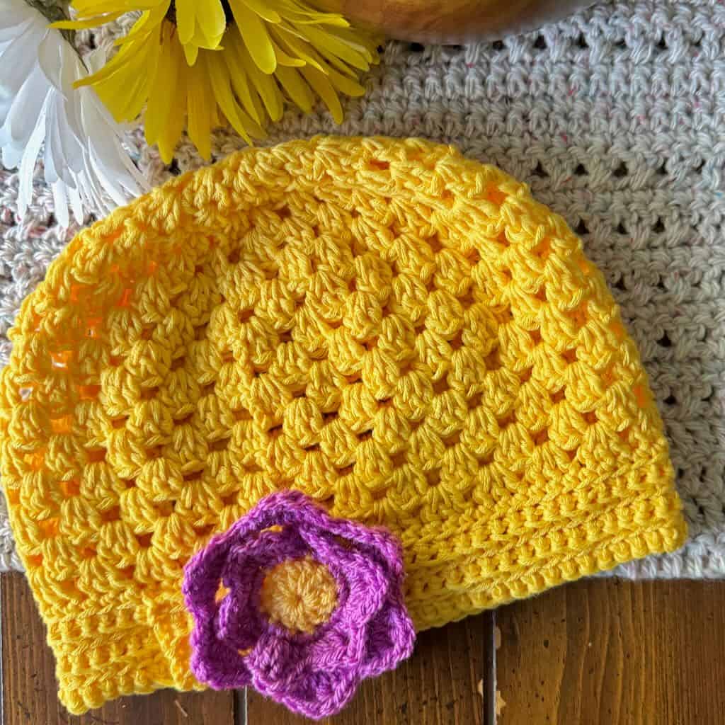 Photo of a granny stitch hat in yellow with flowers in the background