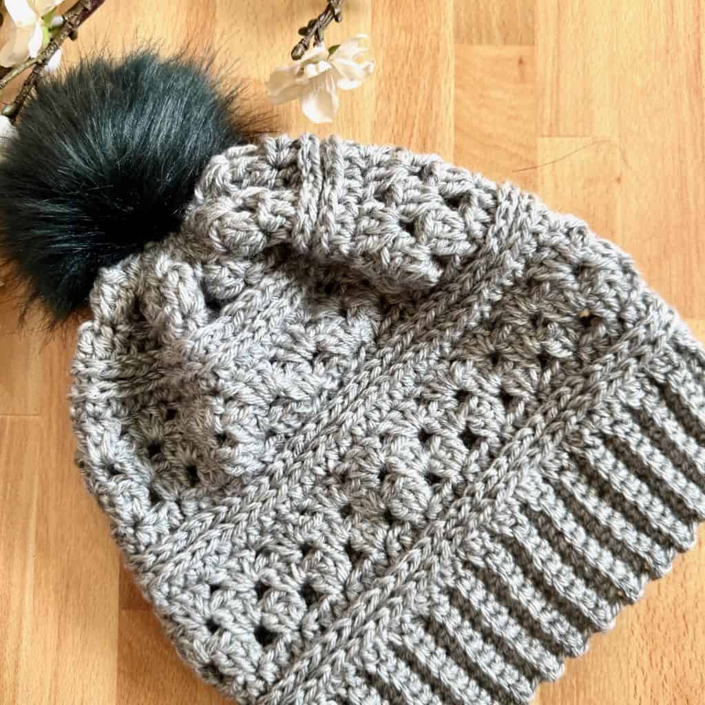 A closeup of the Cordelia granny stitch hat surrounded by flowers on a wooden background